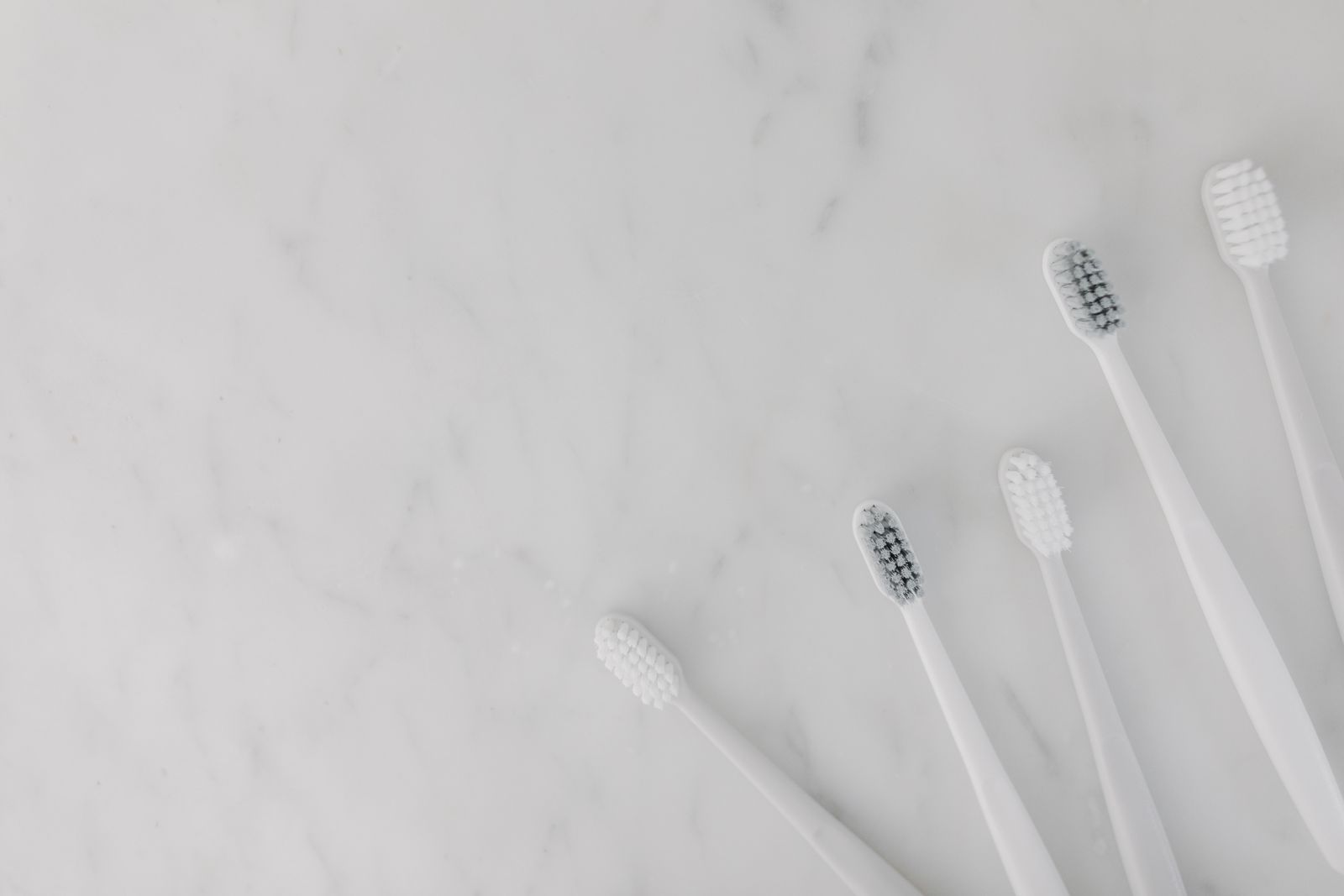 Five white toothbrushes arranged on a pale marble surface